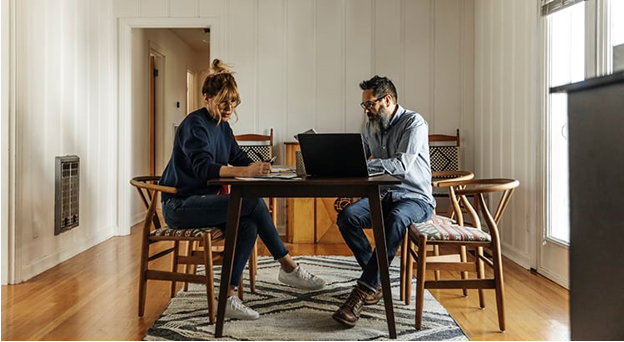 Two people sitting at a table with laptops.